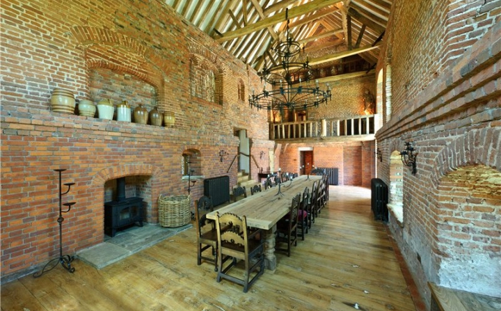 Large Medievil style oak table with twenty chairs in a brick wall room.