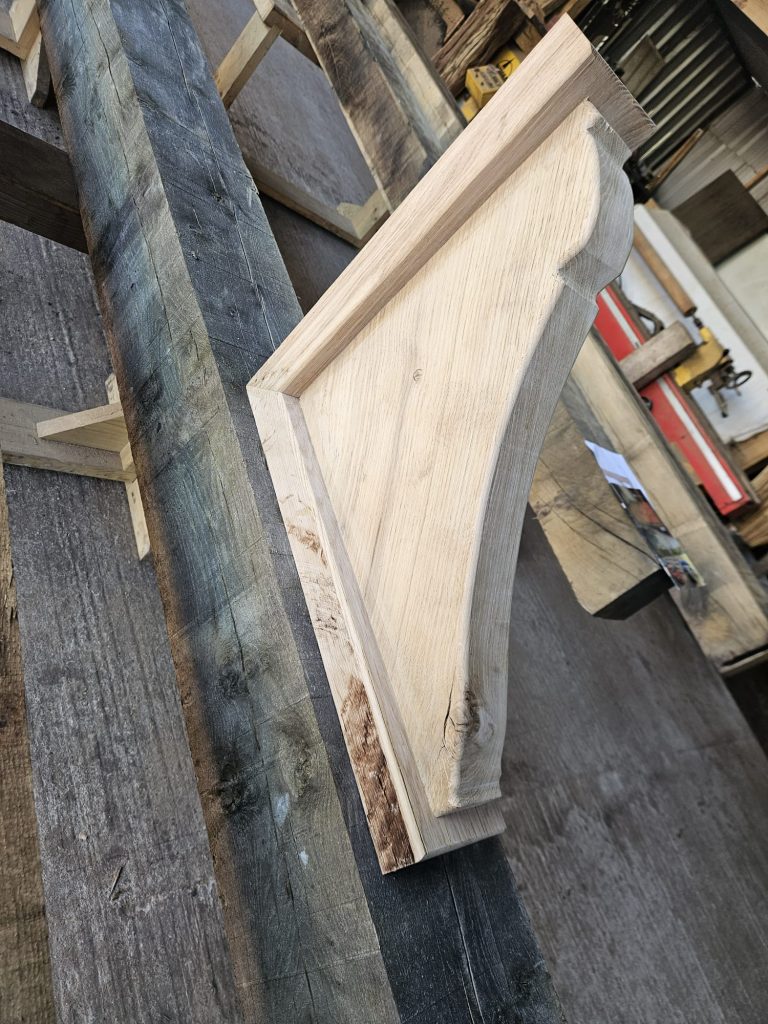 Single unfinished oak corbel with decorative curves, resting on a rustic workbench in a woodworking shop