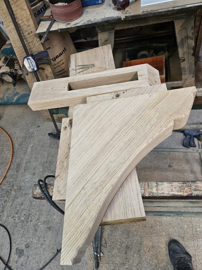 Oak corbel in progress, showing curved profile and clean joinery, clamped to a workbench during construction