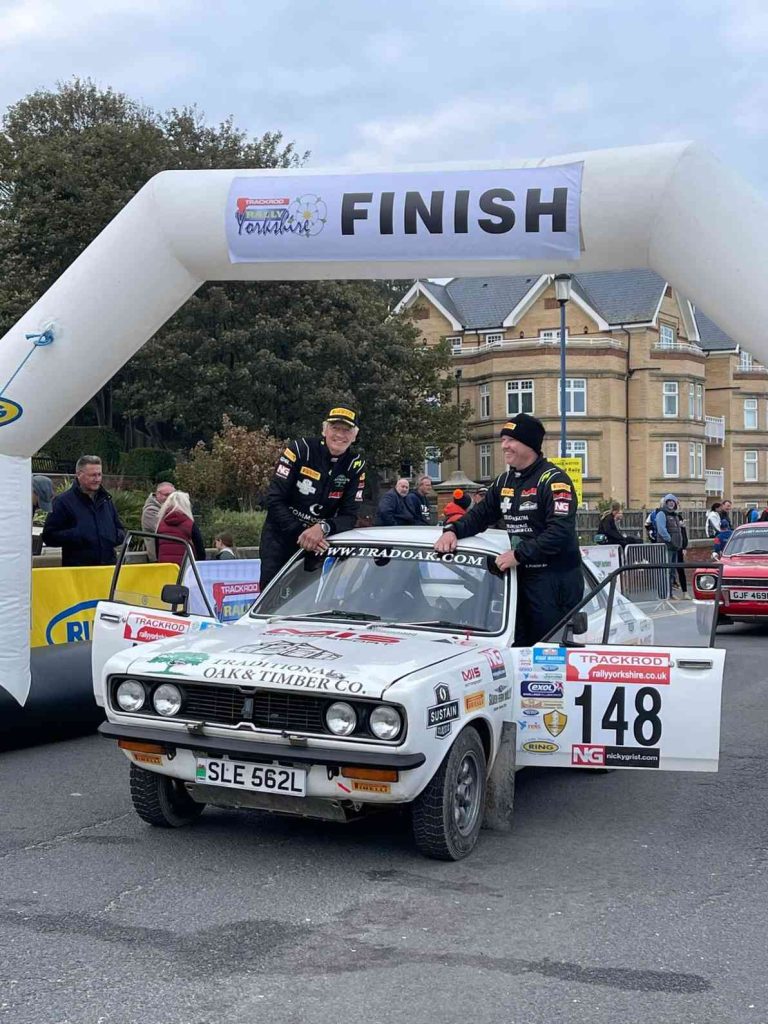 Drivers for Tradoak.com rally team posing with the car at finish line