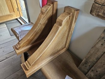 Pair of handcrafted oak corbels with a smooth varnished finish, displayed indoors on a wooden bench